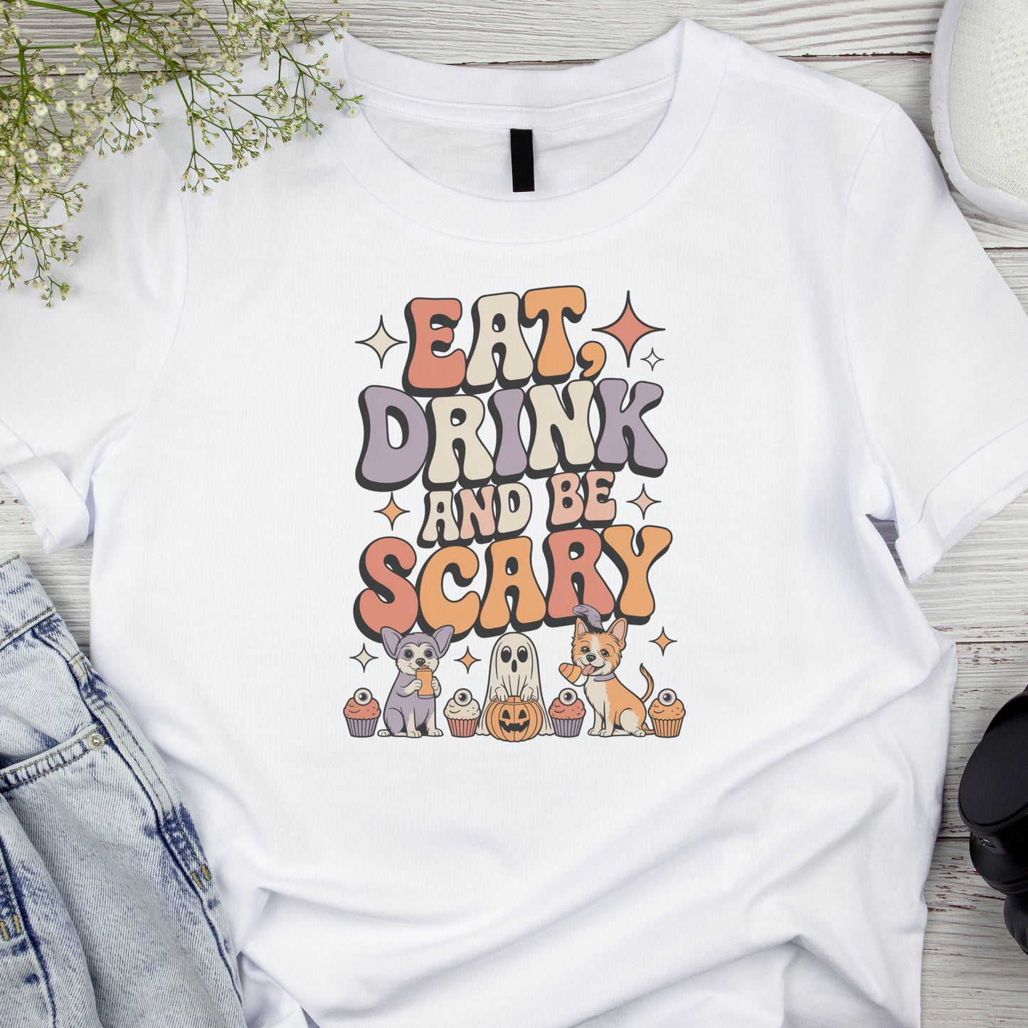 White t-shirt with 'Eat, Drink and Be Scary' Halloween design on a wooden surface.