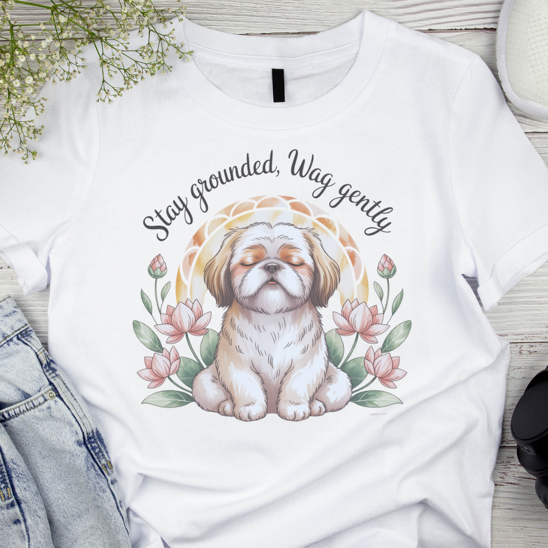 White t-shirt with a dog illustration and text 'Stay grounded, Wag gently' on a wooden surface.
