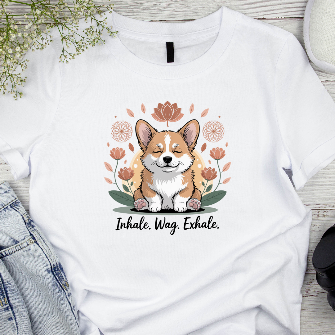 White t-shirt with a corgi graphic and 'Inhale. Wag. Exhale.' text on a wooden surface.
