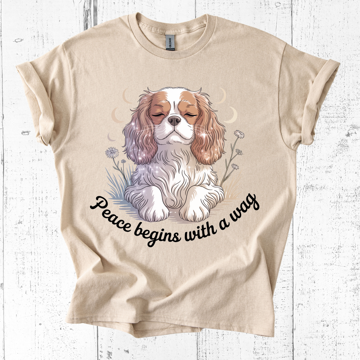 Beige t-shirt with a dog illustration and 'Peace begins with a wag' text on a wooden surface