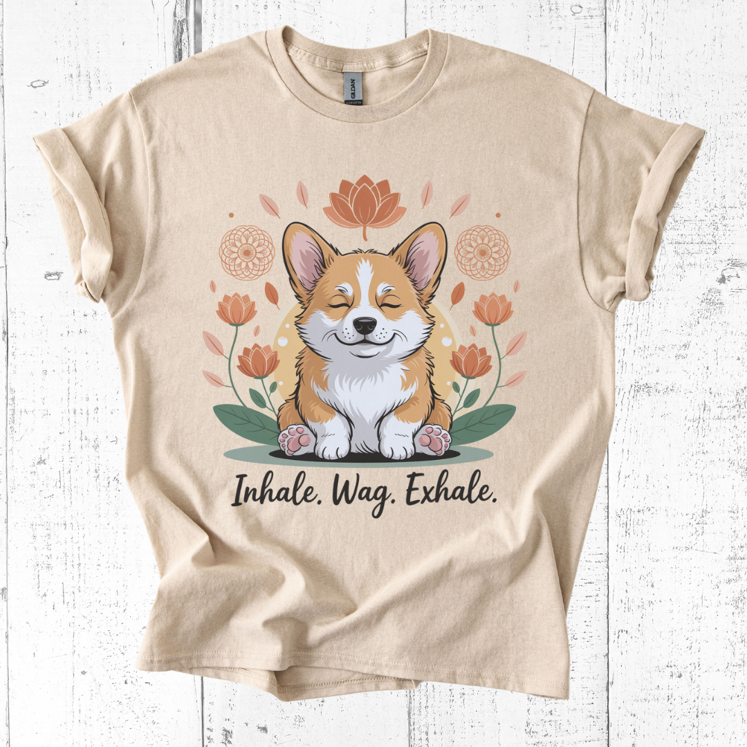 Beige t-shirt with a corgi graphic and 'Inhale. Wag. Exhale.' text on a white wooden background