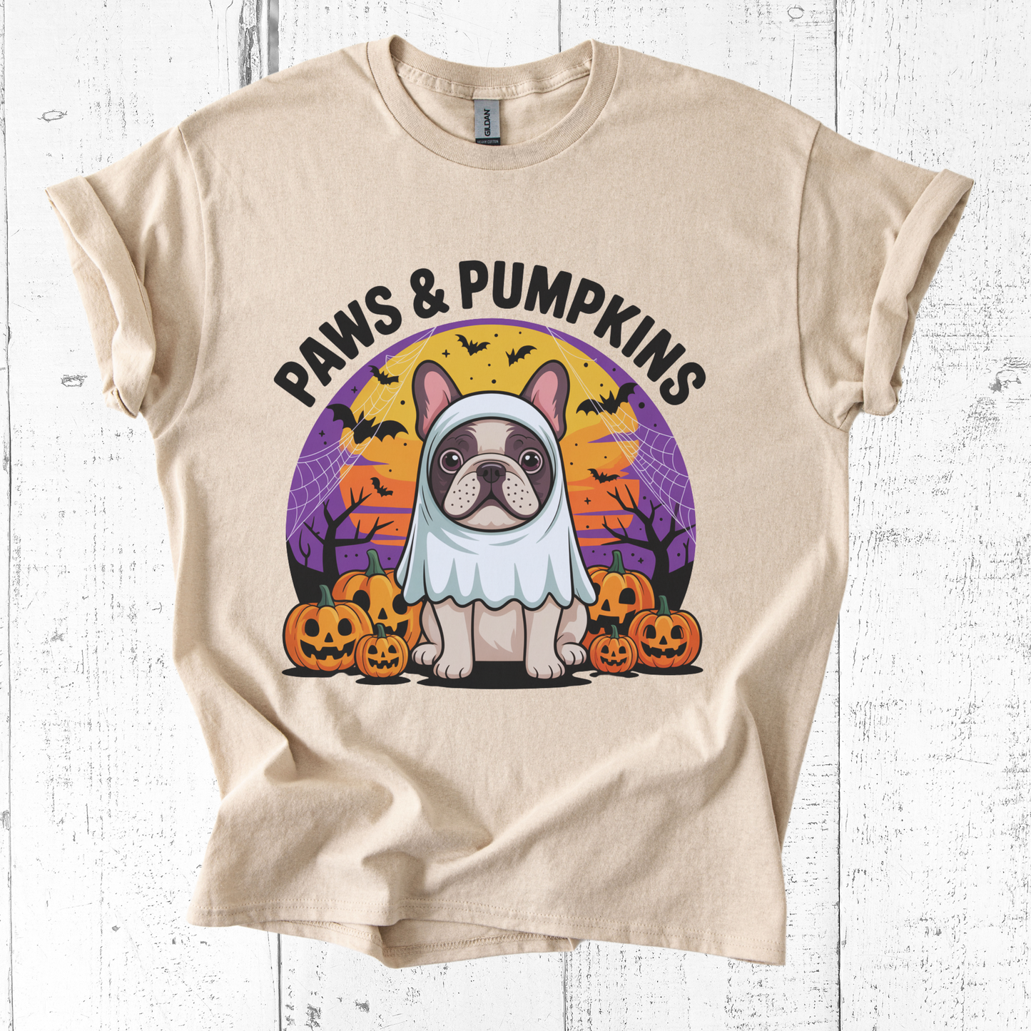 Beige t-shirt with a Halloween-themed graphic of a dog in a ghost costume and pumpkins on a white wooden background.