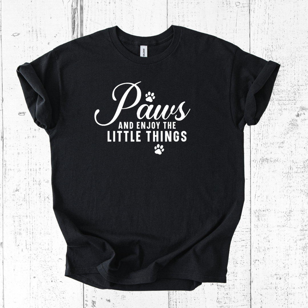 Black t-shirt with white text 'Paws and enjoy the little things' on a wooden surface
