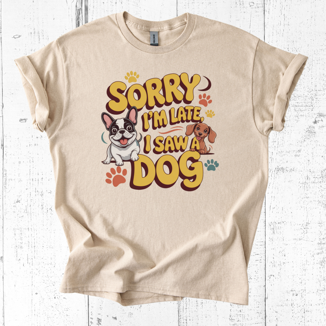 Beige t-shirt with cartoon dogs and text 'Sorry I'm late, I saw a dog' on a white wooden background