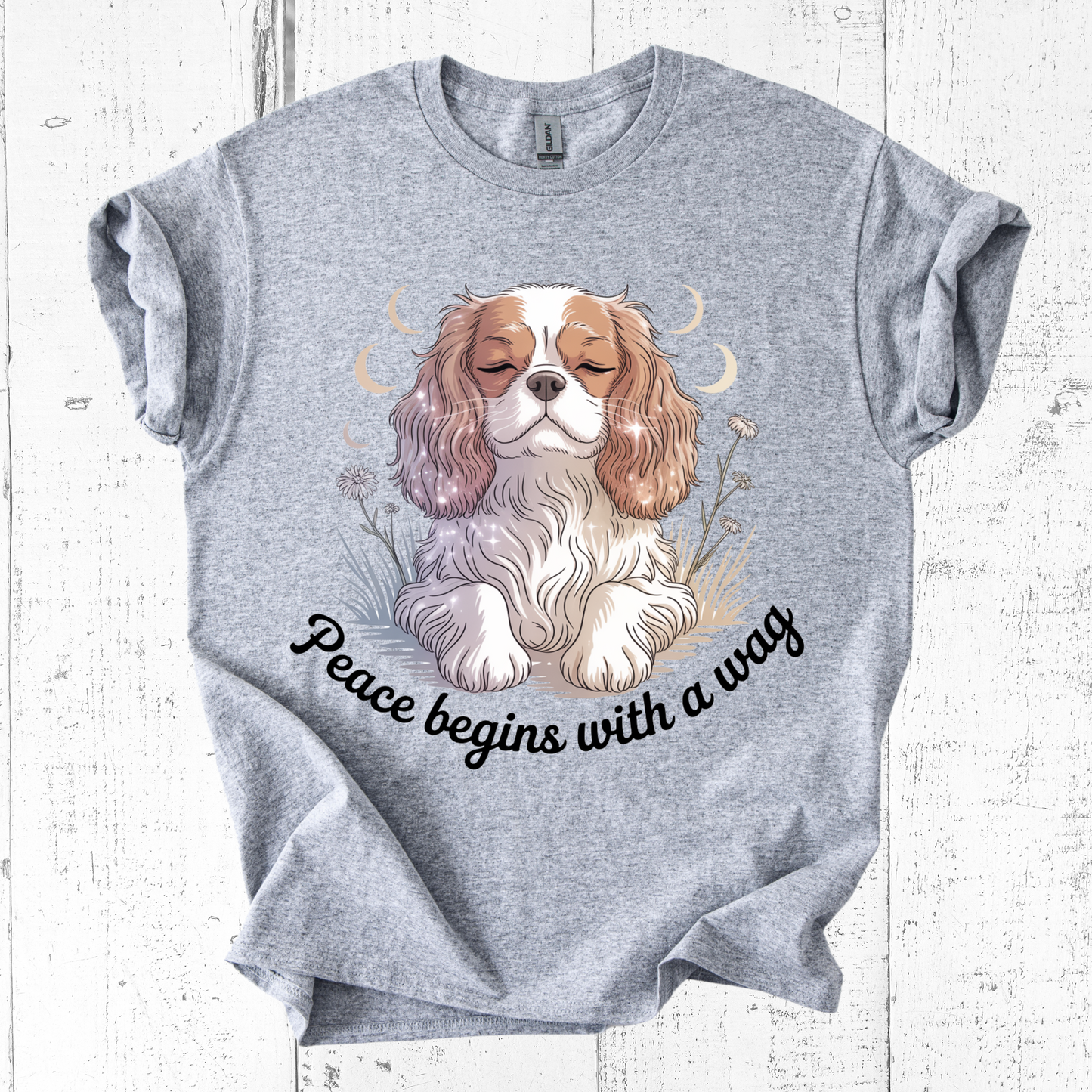 Gray t-shirt with a dog illustration and 'Peace begins with a wag' text on a white wooden background