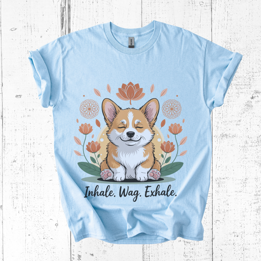 Light blue t-shirt with a corgi graphic and 'Inhale. Wag. Exhale.' text on a wooden surface.