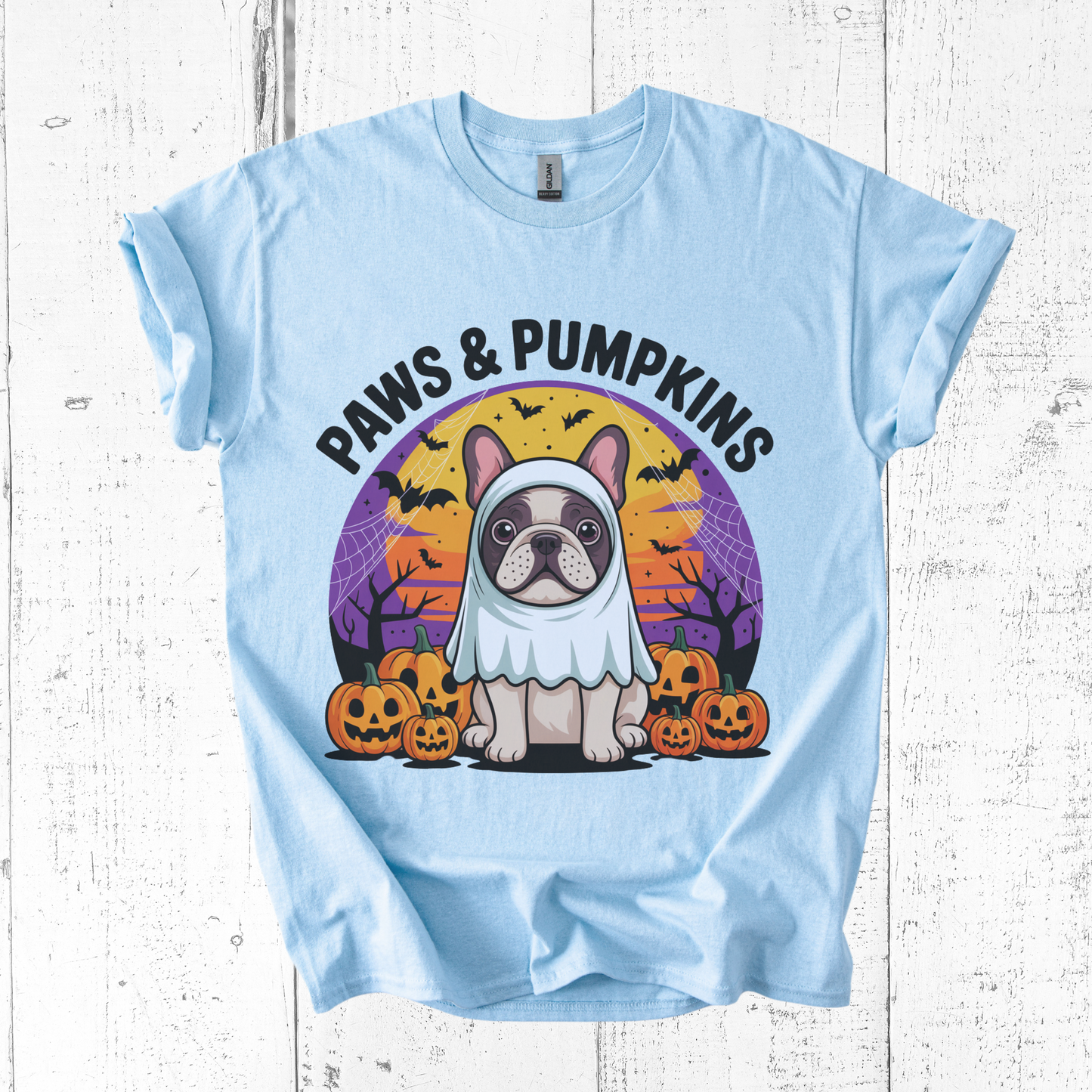 Light blue t-shirt with a Halloween-themed design featuring a dog in a costume and pumpkins on a white wooden background.