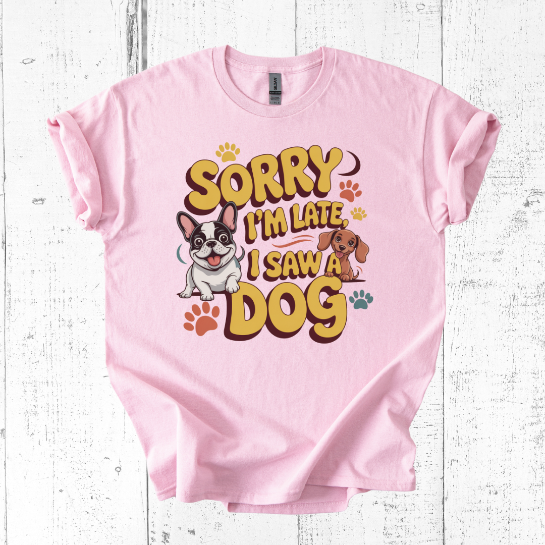Pink t-shirt with cartoon dogs and text 'Sorry I'm late, I saw a dog' on a white wooden background