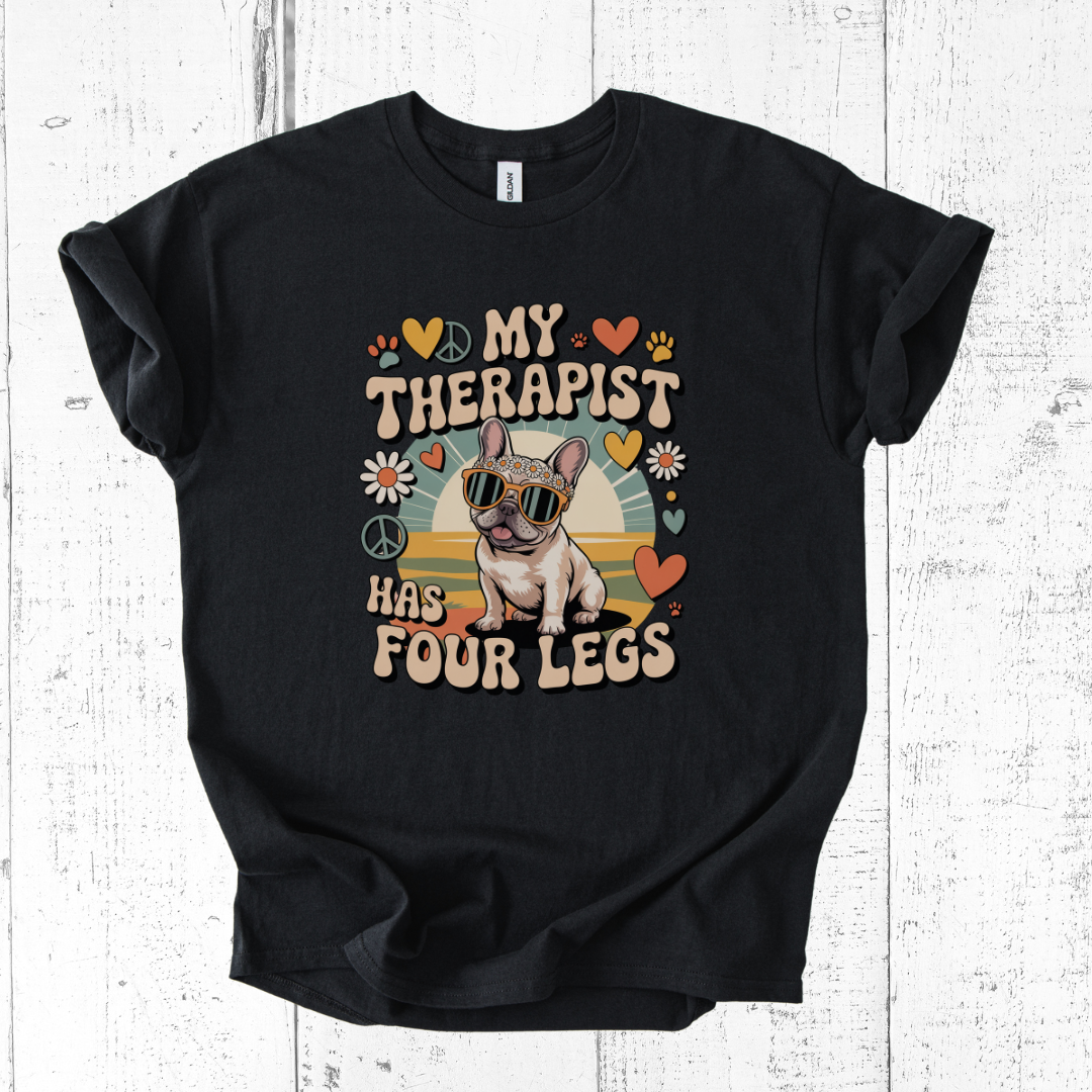 Black t-shirt with a graphic of a dog and text 'My therapist has four legs' on a wooden surface.