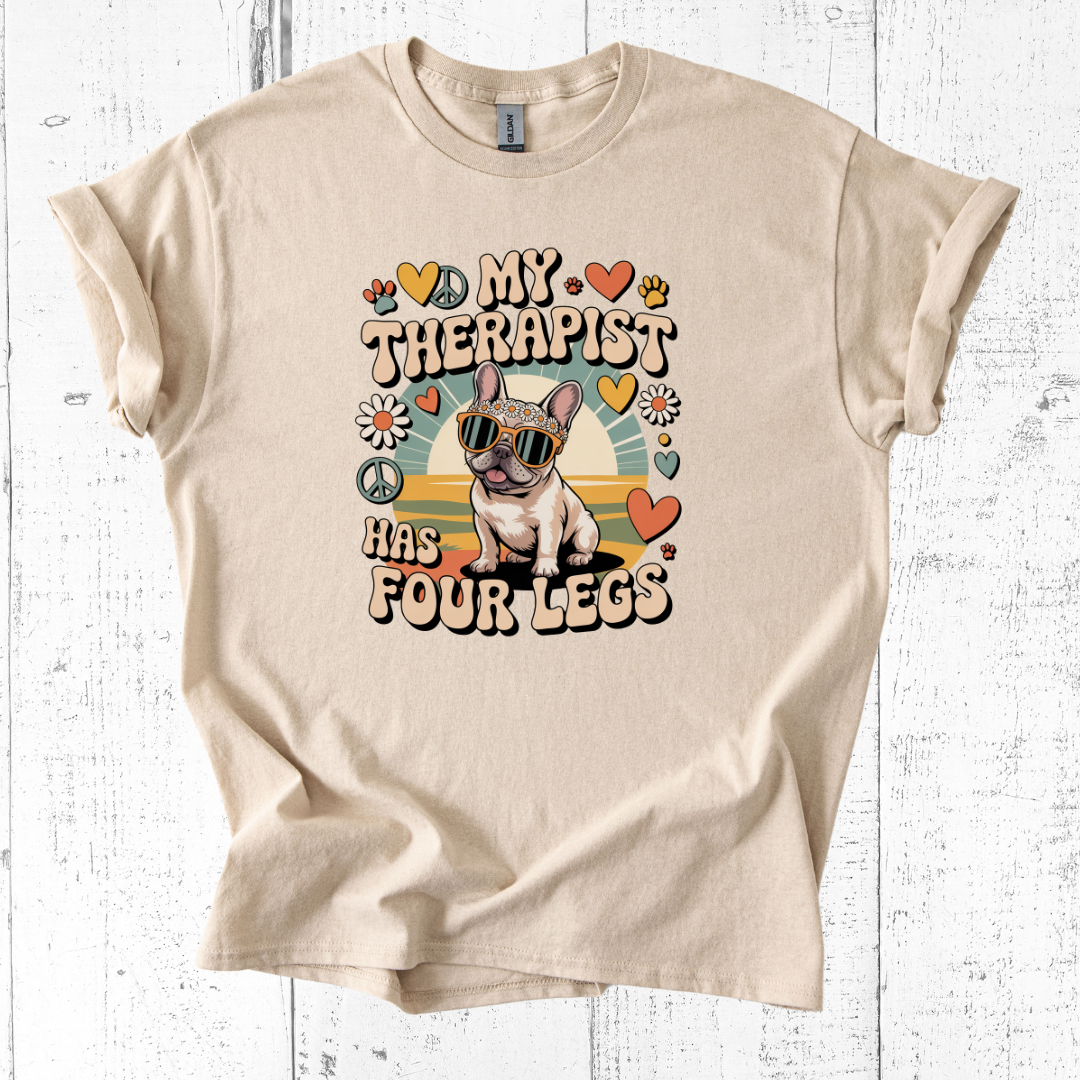 Beige t-shirt with a graphic of a dog and text 'My therapist has four legs' on a white wooden background