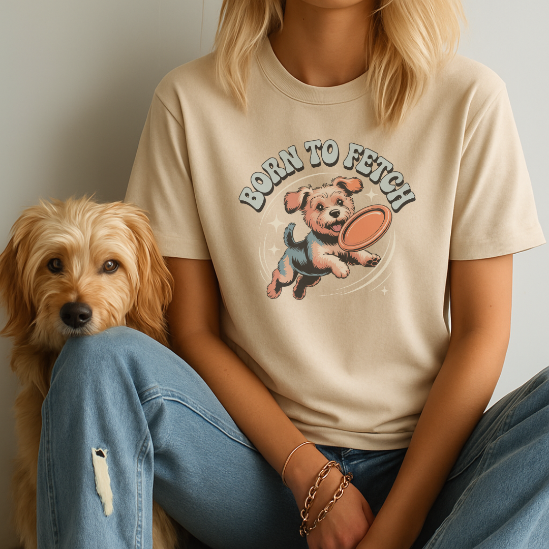 Person wearing a 'Born to Fetch' t-shirt with a dog graphic, sitting next to a small dog.