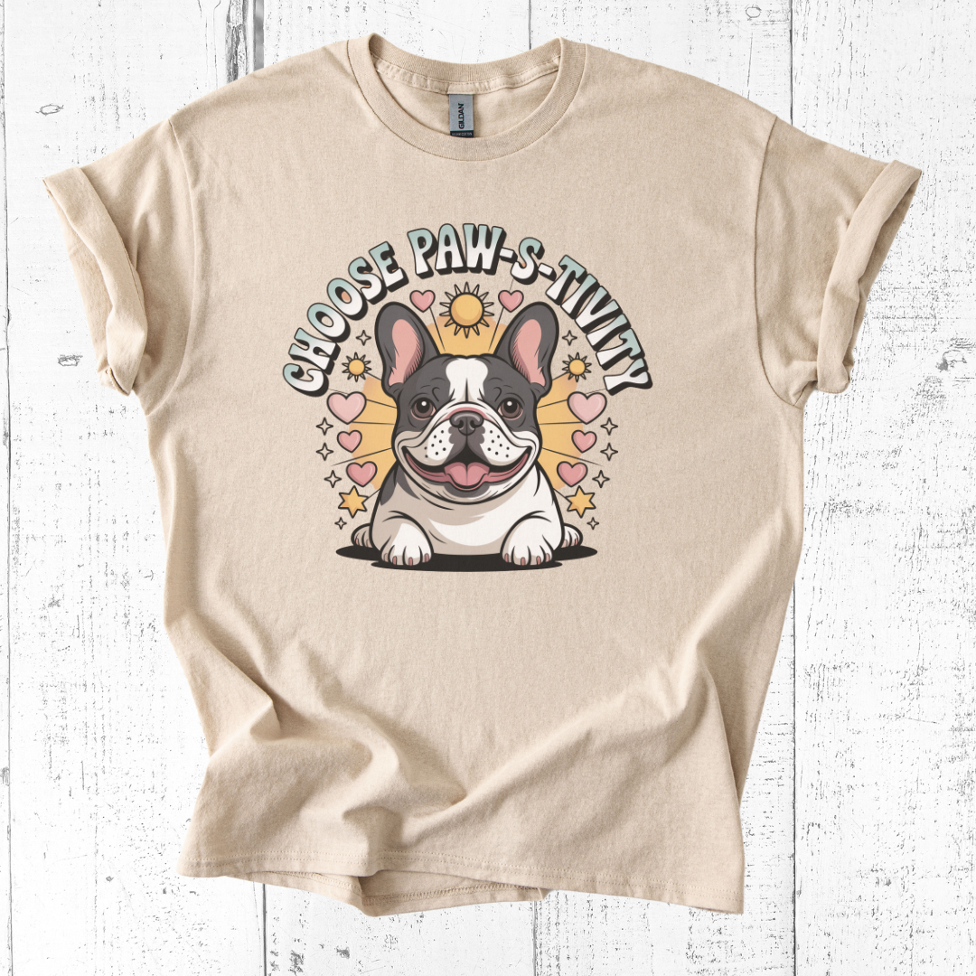 Beige t-shirt with a cartoon dog and 'Choose Paw-sitivity' text on a wooden surface