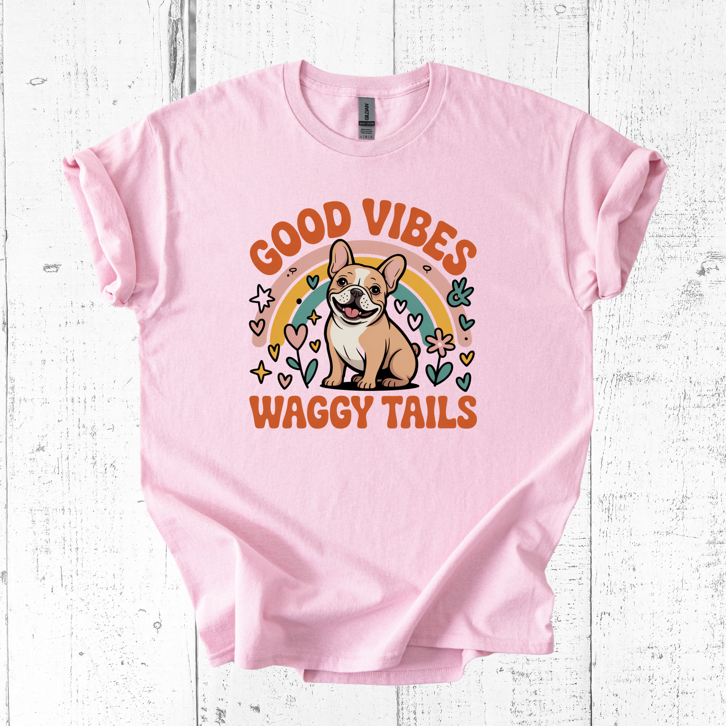 Pink t-shirt with a dog graphic and 'Good Vibes Waggy Tails' text on a white wooden background