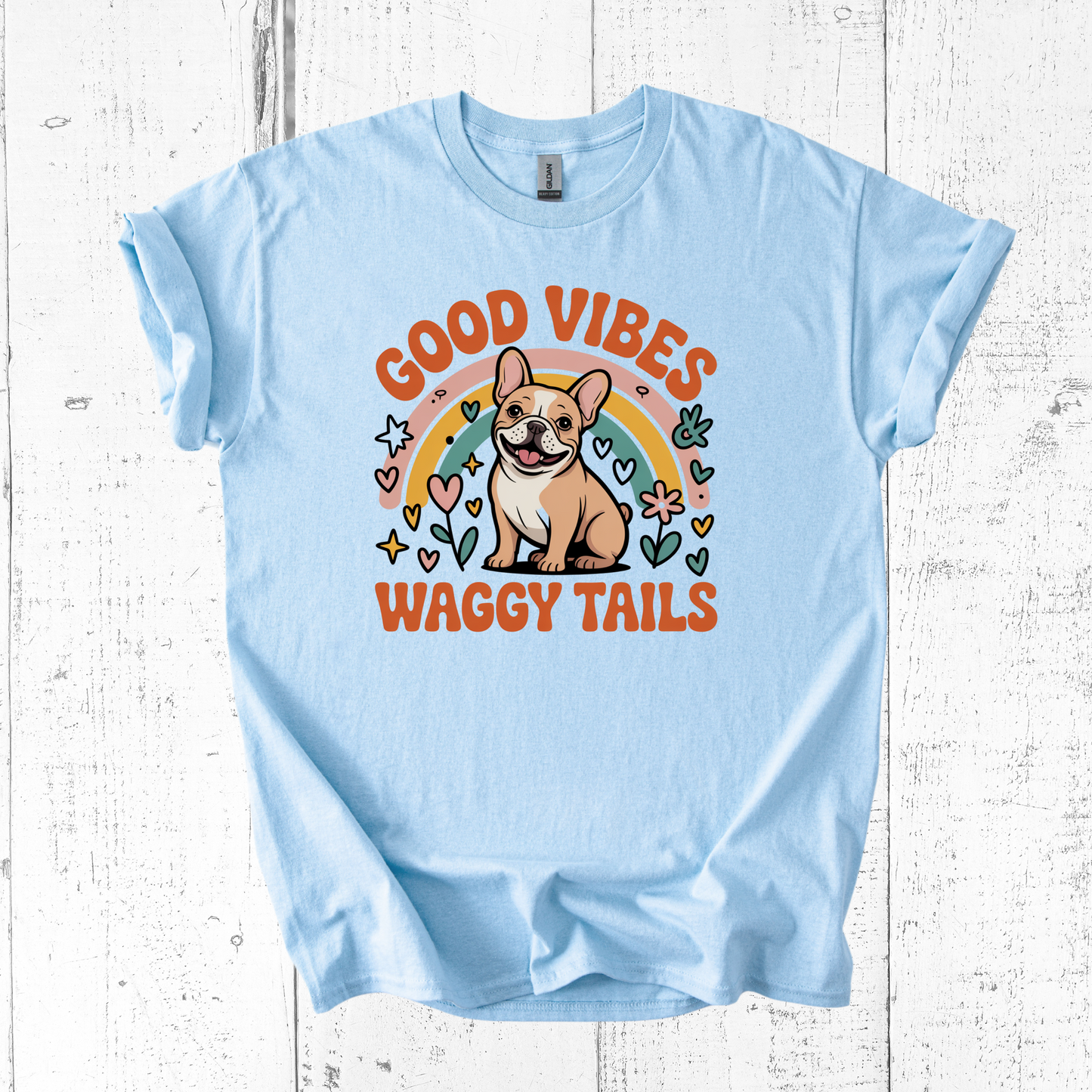 Light blue t-shirt with a dog graphic and text 'Good Vibes Waggy Tails' on a wooden surface.