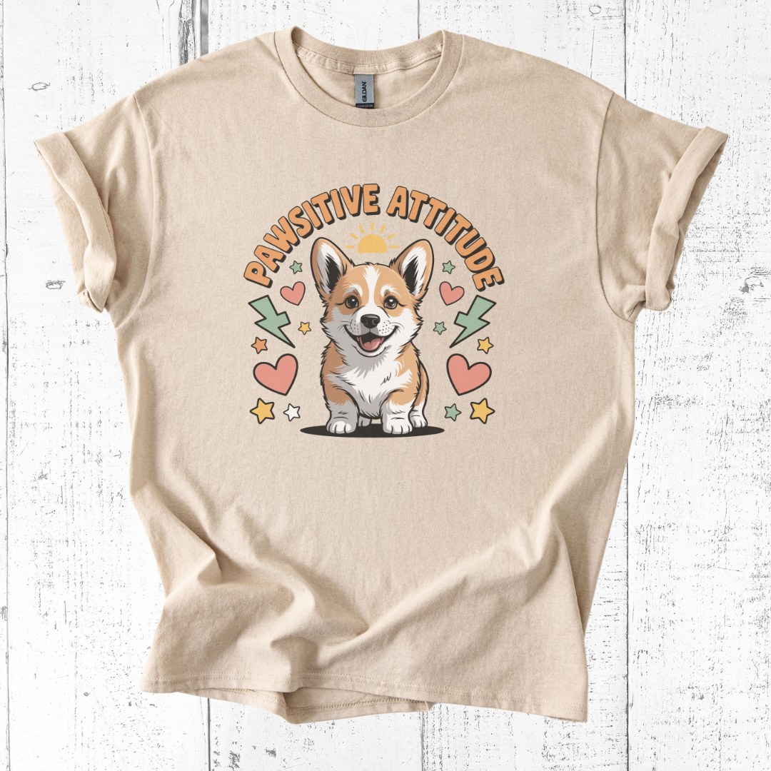 Beige t-shirt with a corgi graphic and 'Pawsitive Attitude' text on a white wooden background