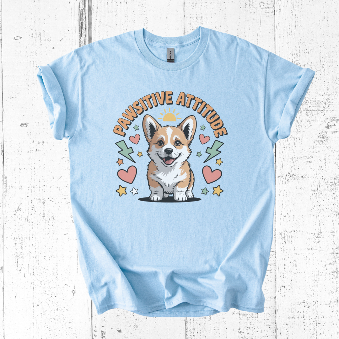 Light blue t-shirt with a corgi graphic and 'Pawsititive Attitude' text on a wooden surface