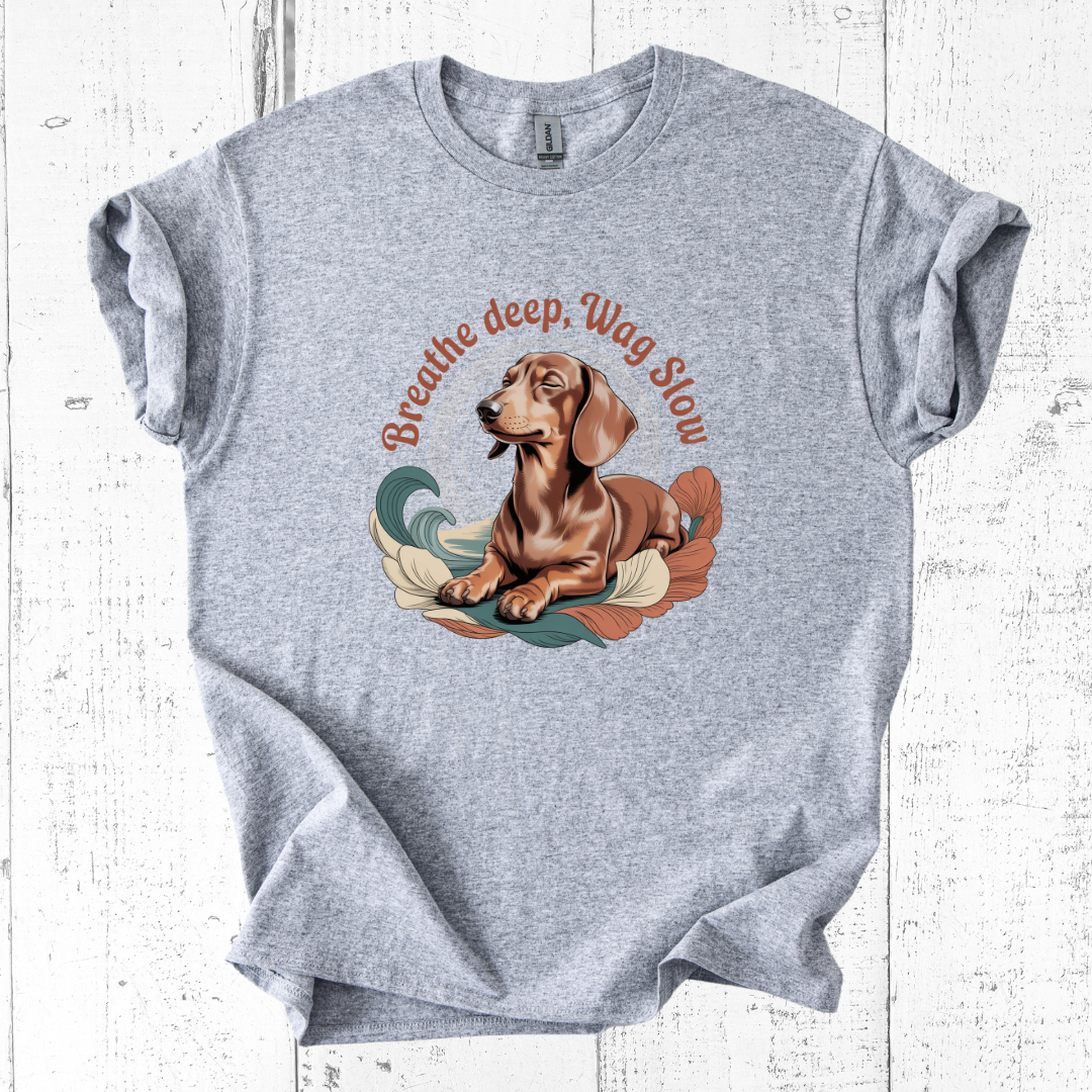 Gray t-shirt with a dachshund graphic and 'Breathe deep, Wag Slow' text on a white wooden background