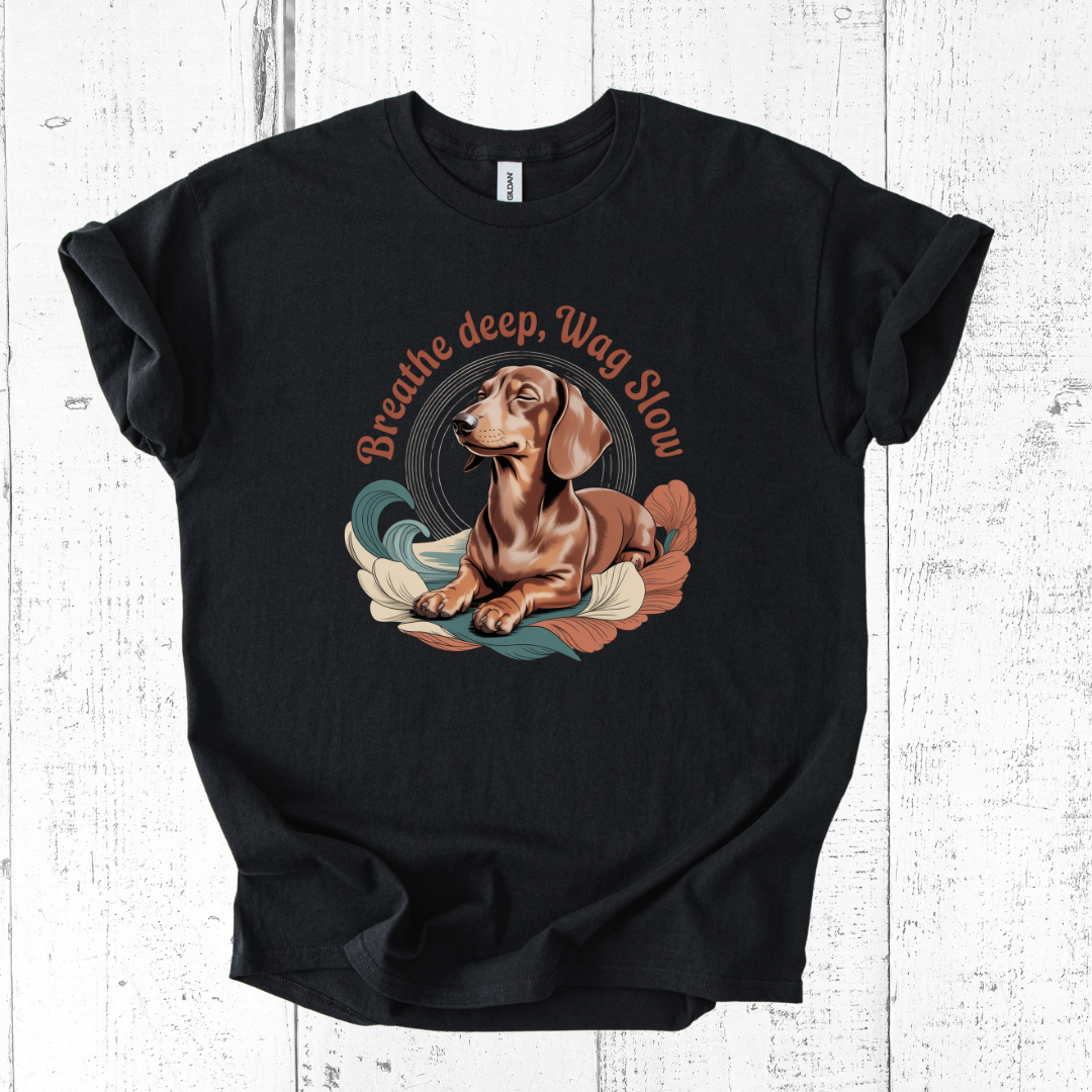 Black t-shirt with a dachshund graphic and 'Breathe deep, Wag slow' text on a wooden surface
