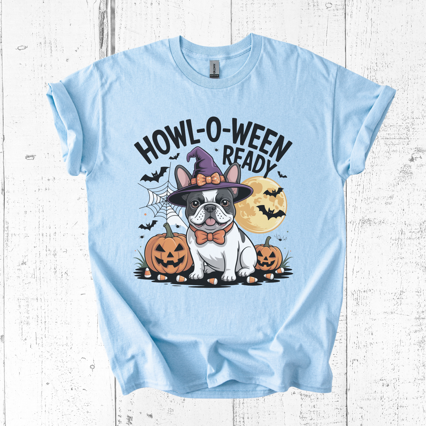 Light blue t-shirt with Halloween-themed design featuring a dog in a witch hat and pumpkins on a white wooden background.