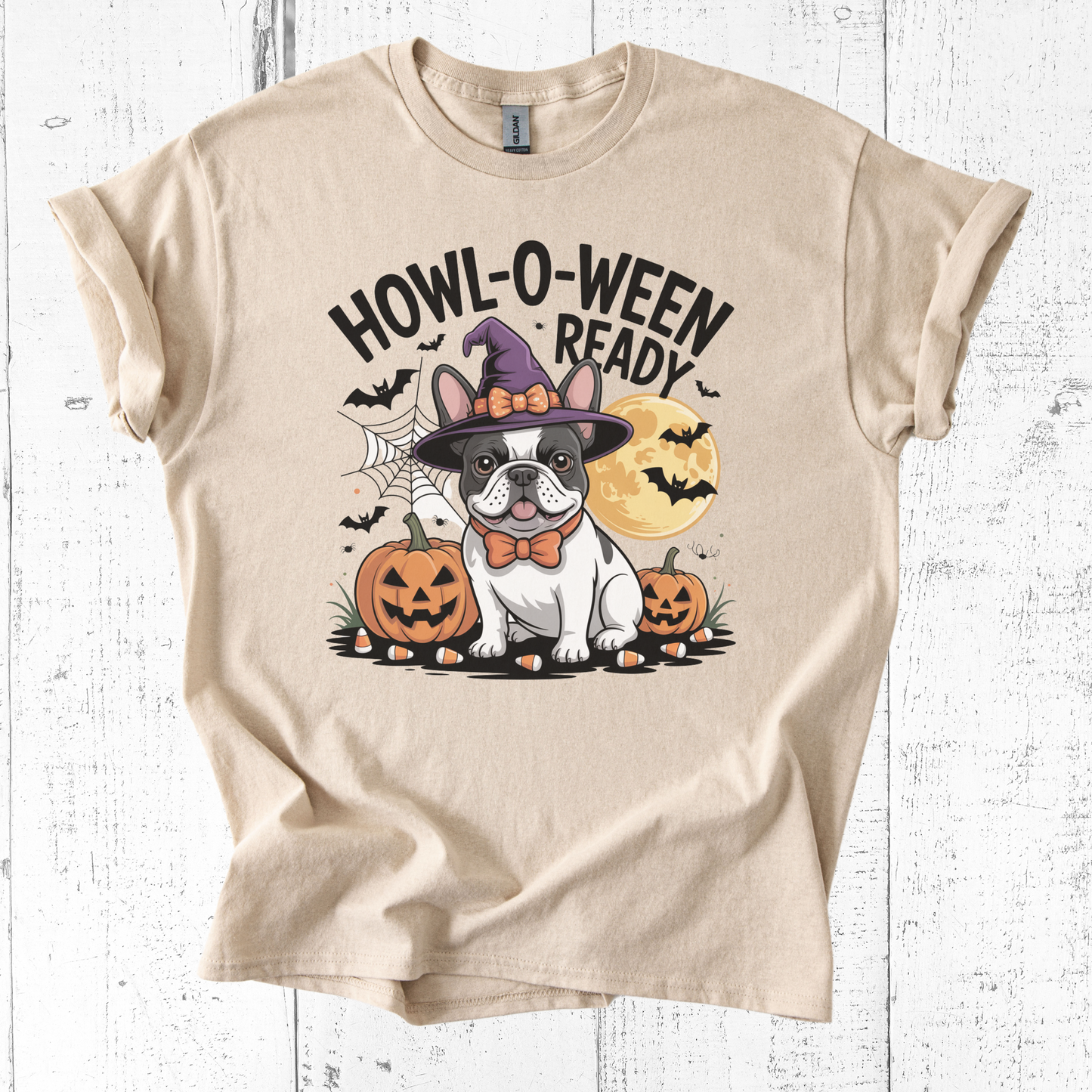 Beige t-shirt with Halloween-themed design featuring a dog in a witch hat and pumpkins on a white wooden background.