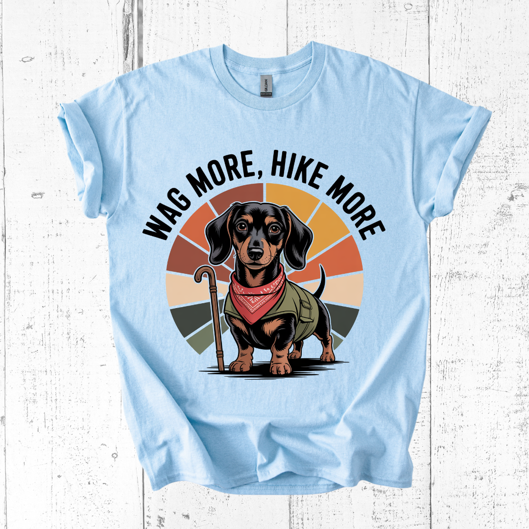 Light blue t-shirt with a dachshund graphic and 'Wag More, Hike More' text on a wooden surface.
