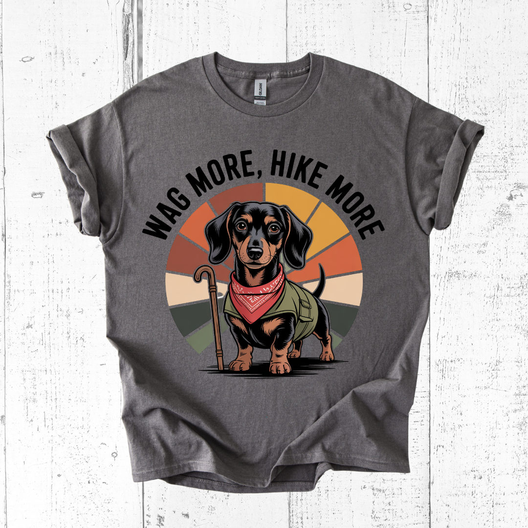 Gray t-shirt with a dachshund graphic and 'Wag More, Hike More' text on a white wooden background