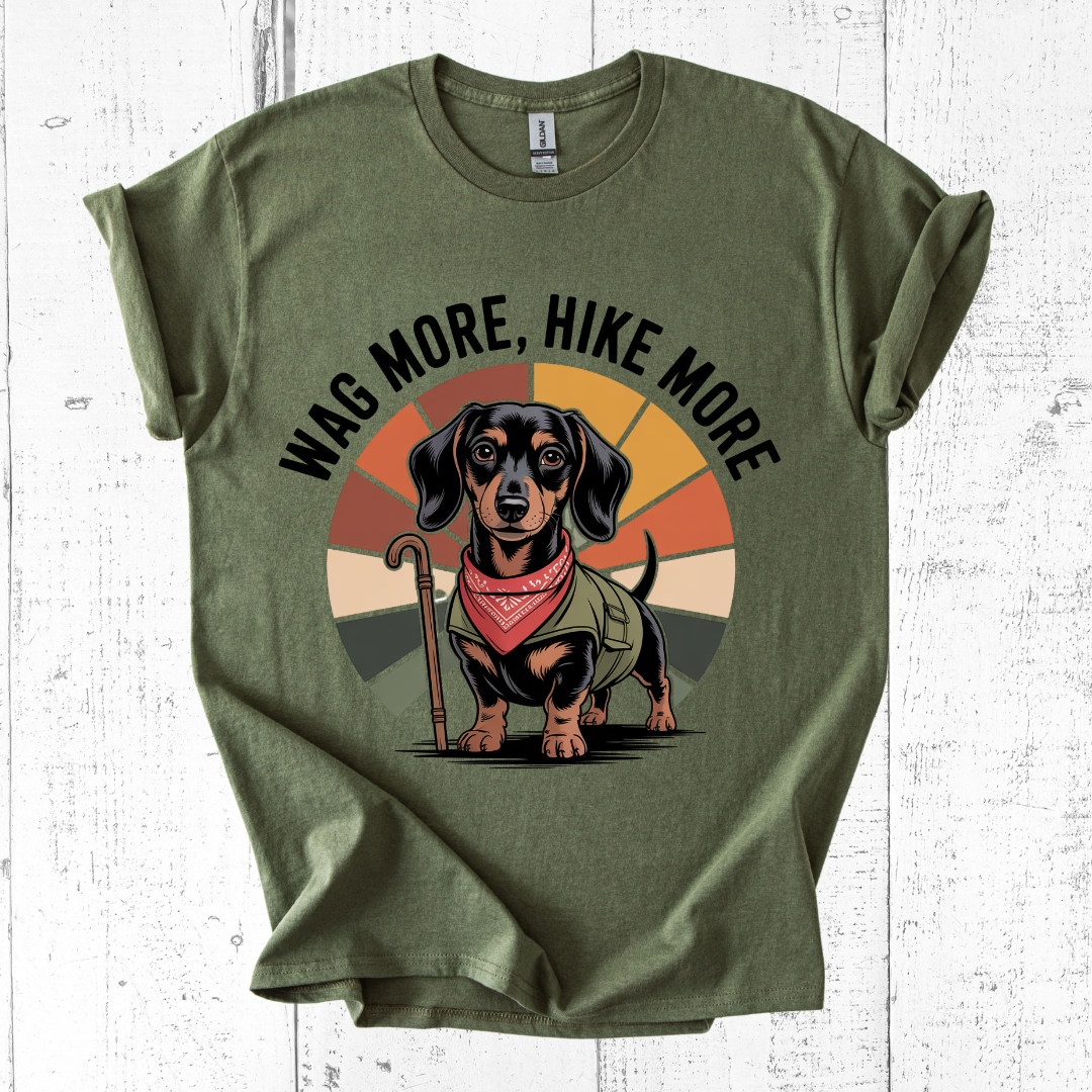 Green t-shirt with a dachshund graphic and 'Wag More, Hike More' text on a white wooden background