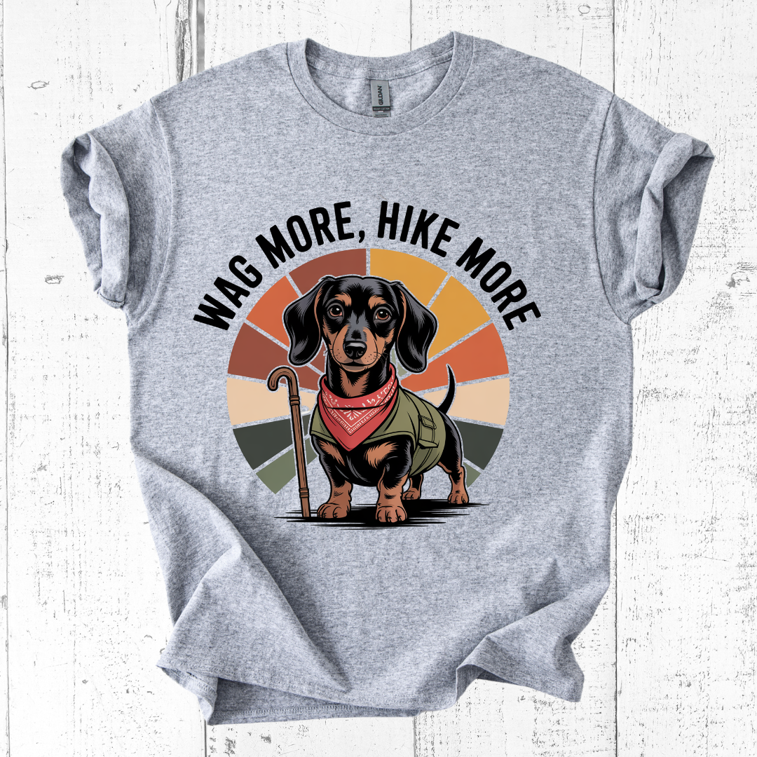 Gray t-shirt with a dachshund graphic and 'Wag More, Hike More' text on a white wooden background