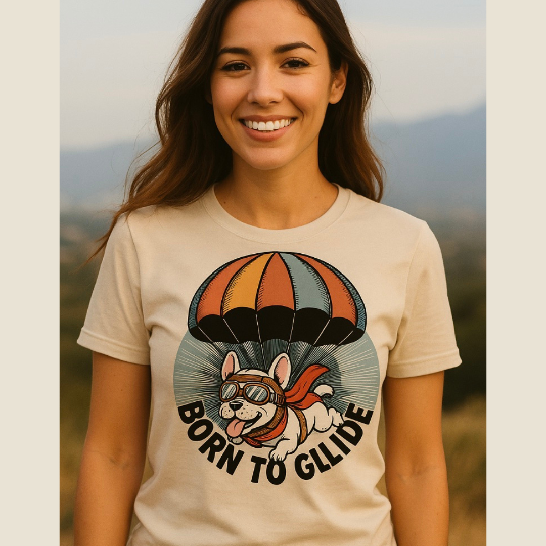 Woman wearing a t-shirt with a graphic of a dog on a parachute and 'Born to Glide' text, standing outdoors.