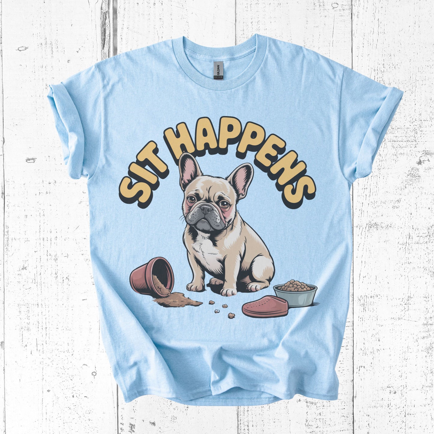 Light blue t-shirt with a cartoon dog and 'SIT HAPPENS' text on a wooden surface