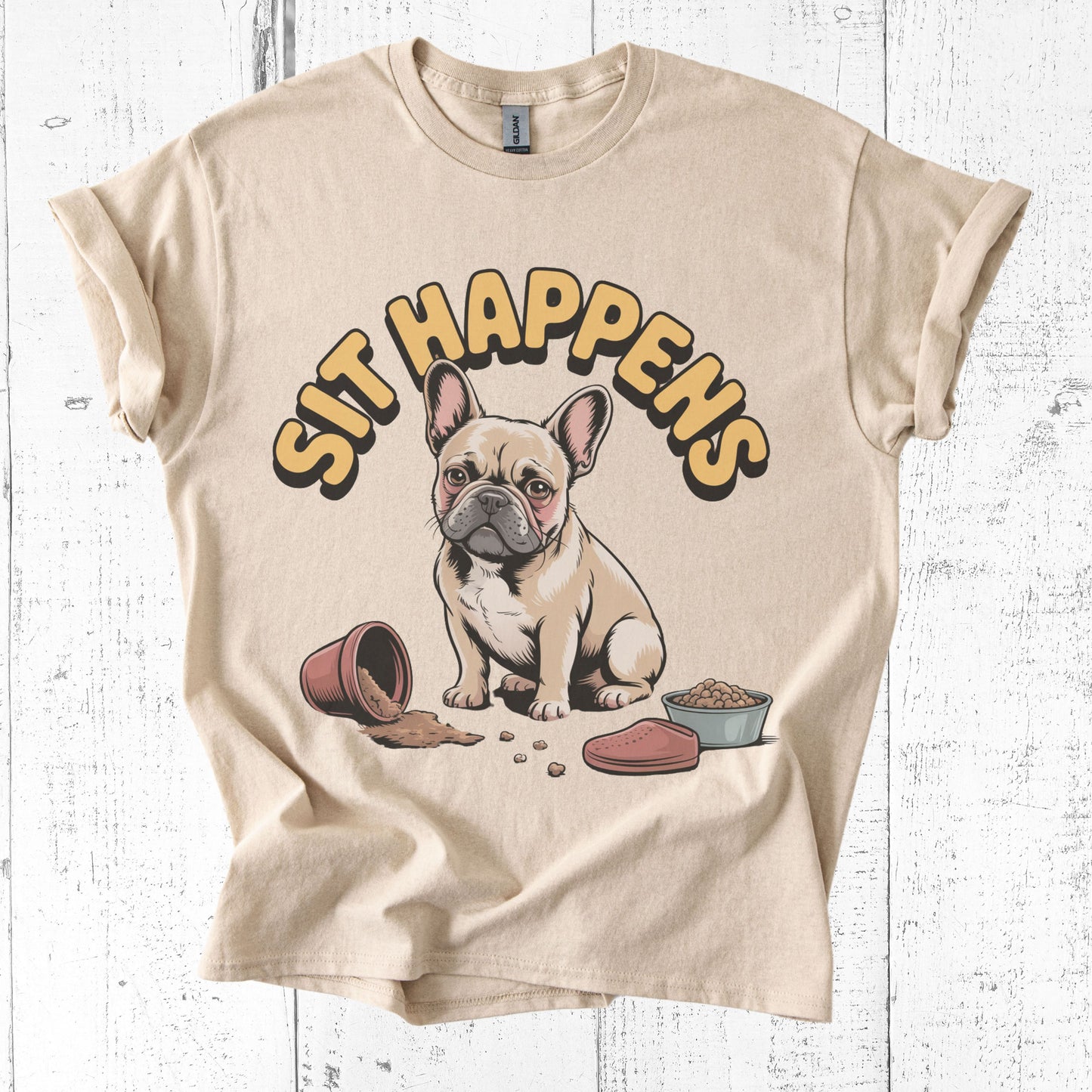 Beige t-shirt with a cartoon dog and 'Sit Happens' text on a white wooden background