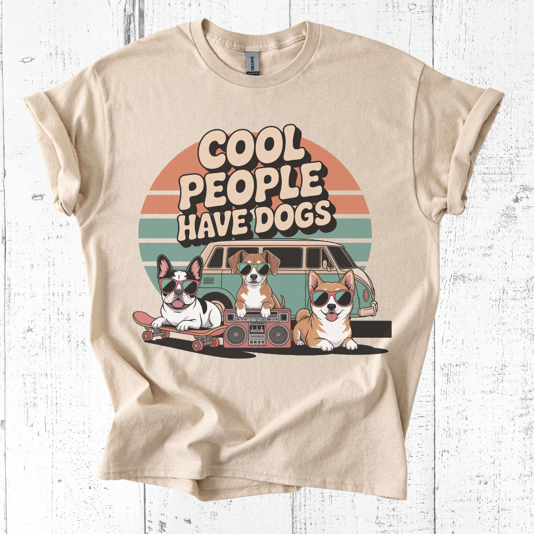 Beige t-shirt with graphic of dogs and 'Cool people have dogs' text on a white wooden background