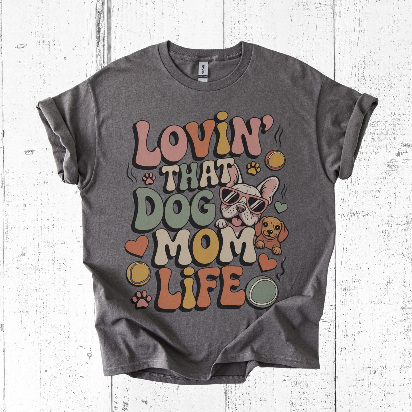 Gray t-shirt with colorful 'Lovin' That Dog Mom Life' graphic on a white wooden surface