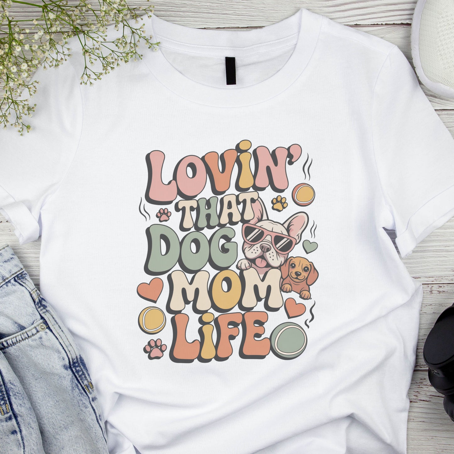 White t-shirt with 'Lovin' that Dog Mom Life' graphic design on a wooden surface.