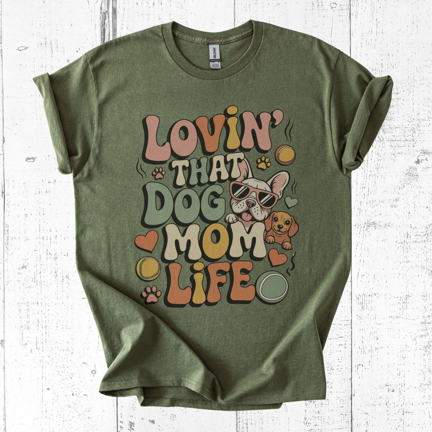 Green t-shirt with 'Lovin' That Dog Mom Life' text and dog graphics on a white wooden background