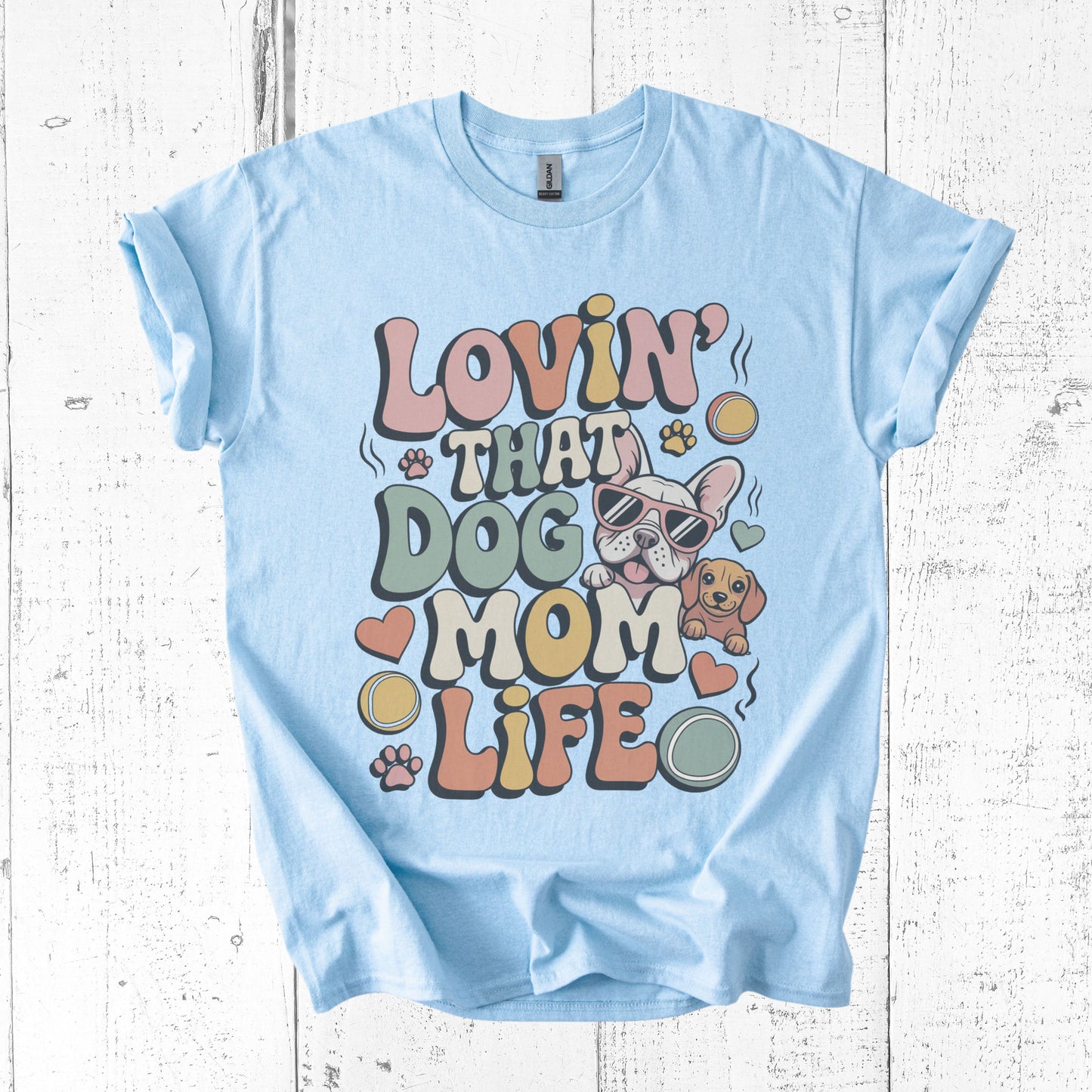 Light blue t-shirt with 'Lovin' That Dog Mom Life' graphic on a white wooden background