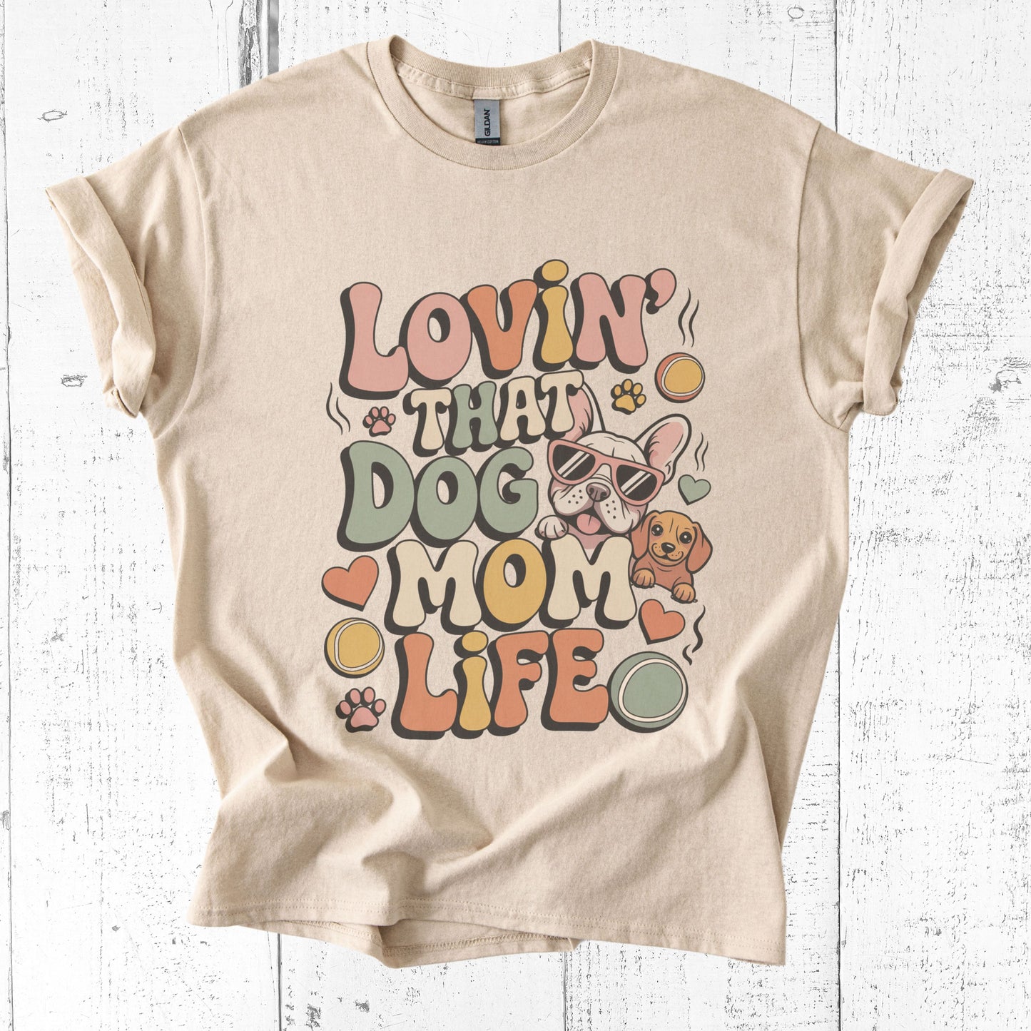 Beige t-shirt with 'Lovin' That Dog Mom Life' graphic on a white wooden background