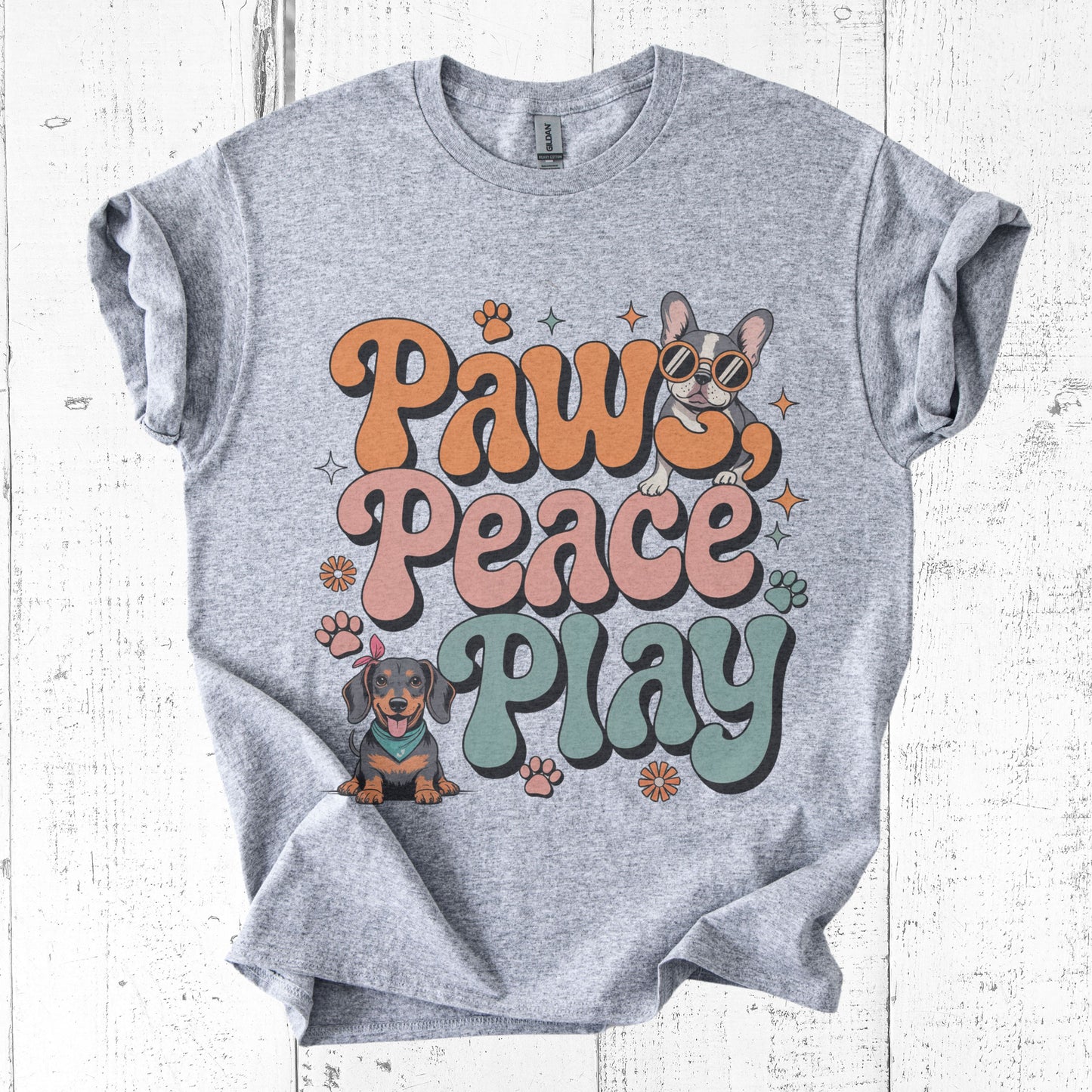 Gray t-shirt with 'Paws Peace Play' text and dog illustrations on a white wooden background