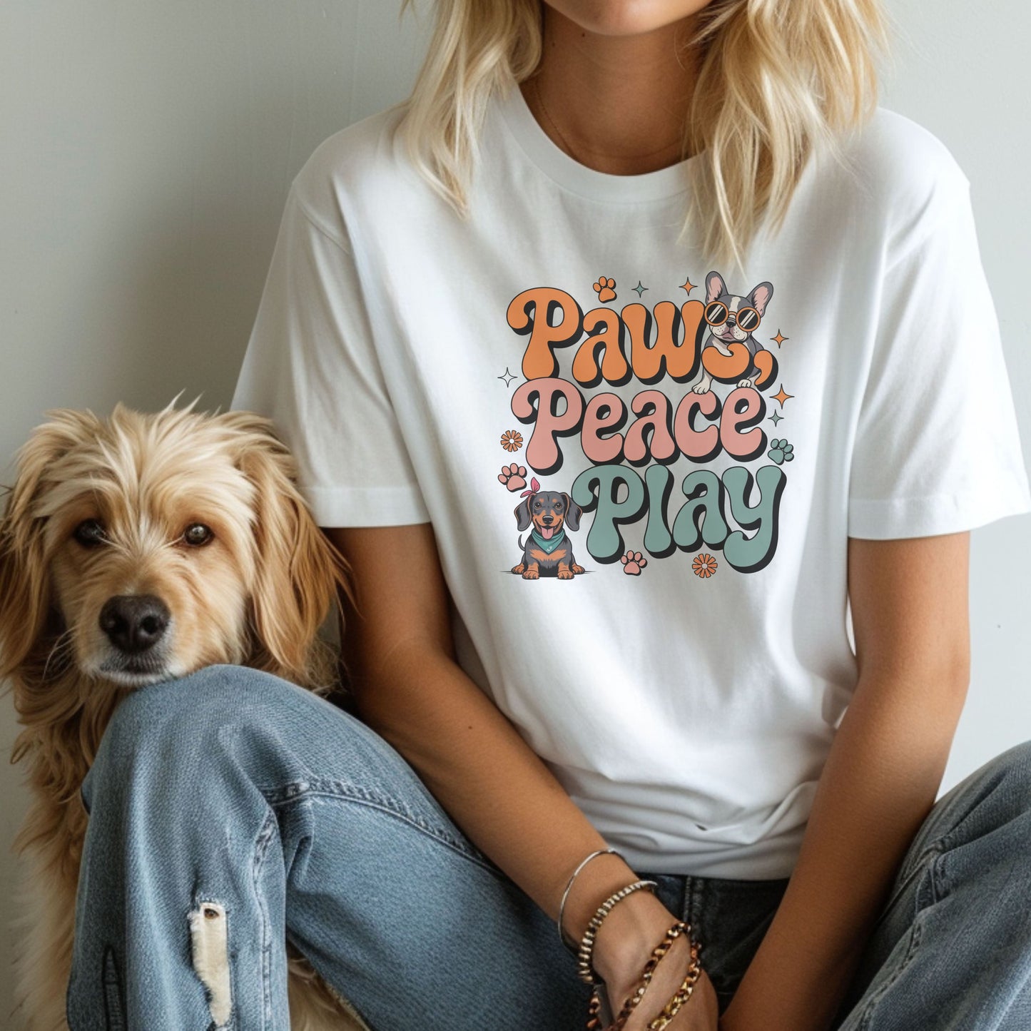 Person wearing a white t-shirt with 'Paws, Peace, Play' design sitting next to a dog.