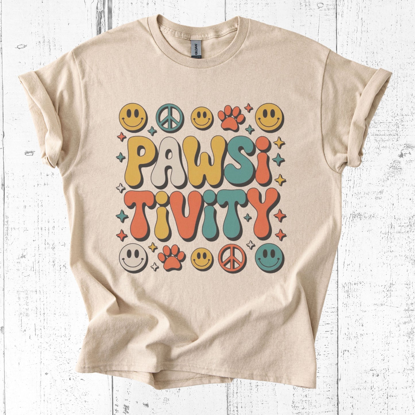 Beige t-shirt with 'PAWSITIVITY' design on a white wooden background