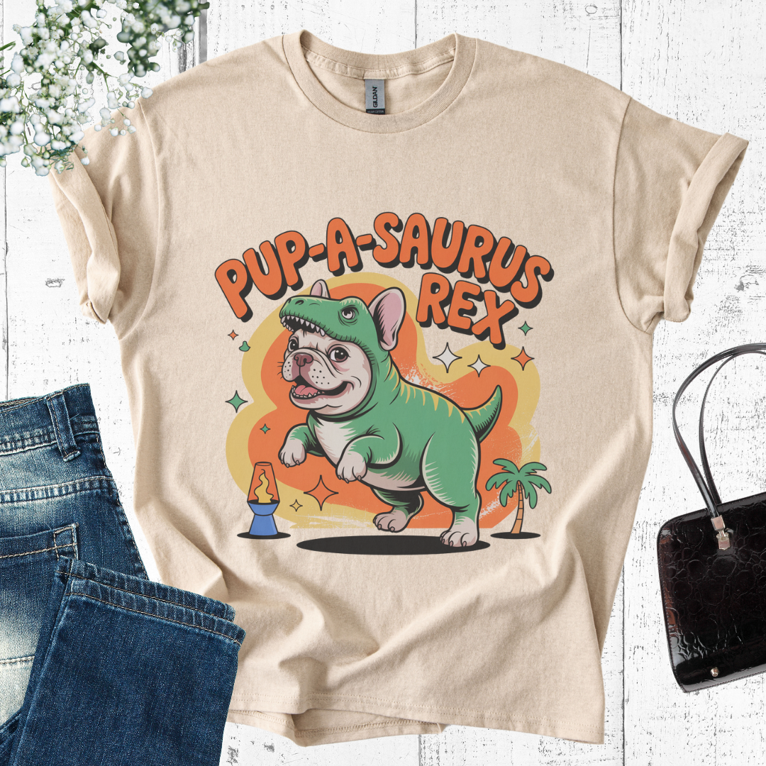 Beige t-shirt with a cartoon dog in a dinosaur costume and 'Pup-A-Saurus Rex' text, displayed with jeans and a handbag.