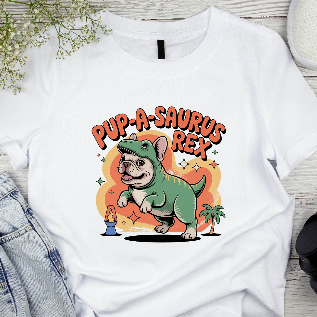 White t-shirt with a cartoon dog dinosaur design and 'Pup-A-Saurus Rex' text on a wooden surface.