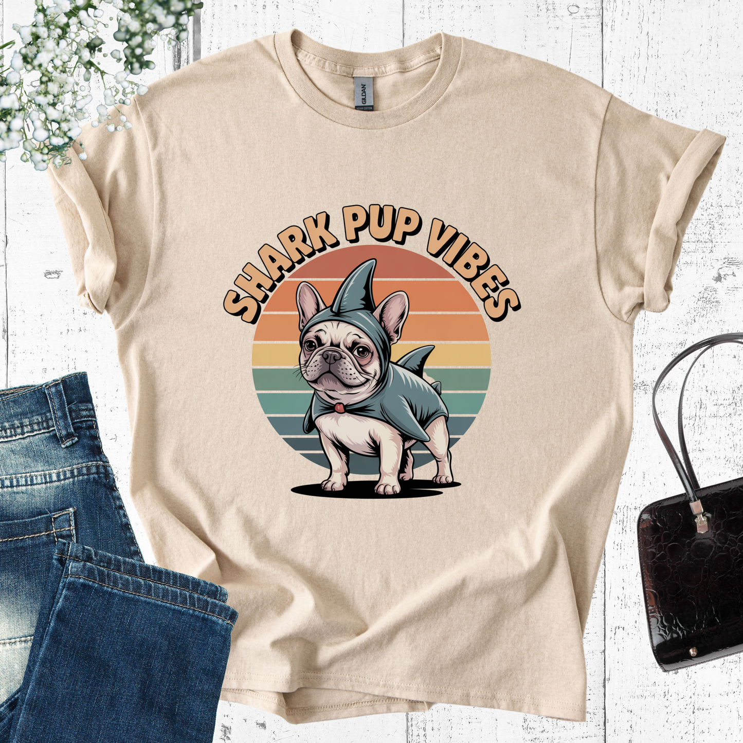 Beige t-shirt with a dog in a shark costume graphic and 'Shark Pup Vibes' text, displayed with jeans and a handbag.