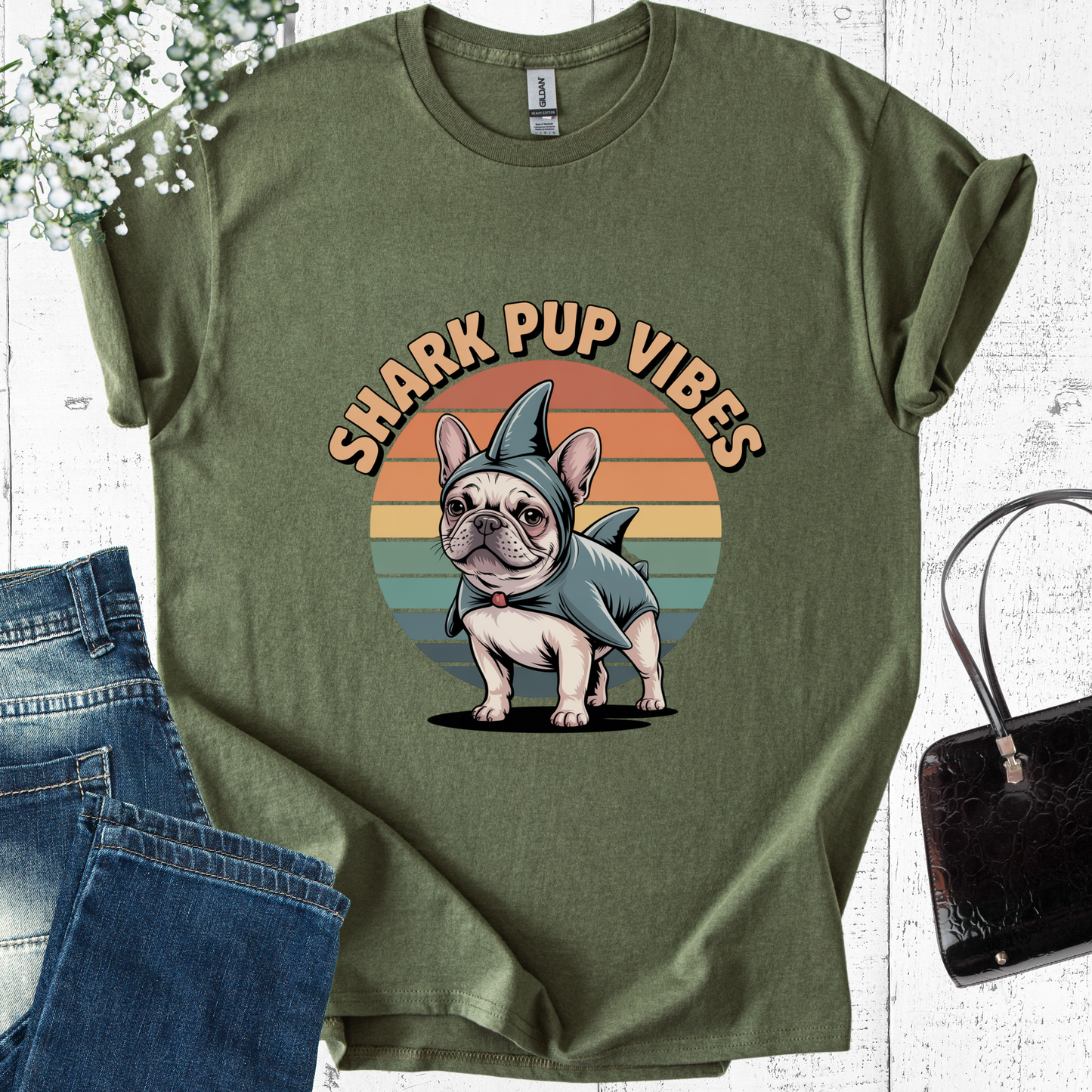 Green t-shirt with a dog in a shark costume graphic and 'Shark Pup Vibes' text, placed on a white surface with jeans and a handbag.