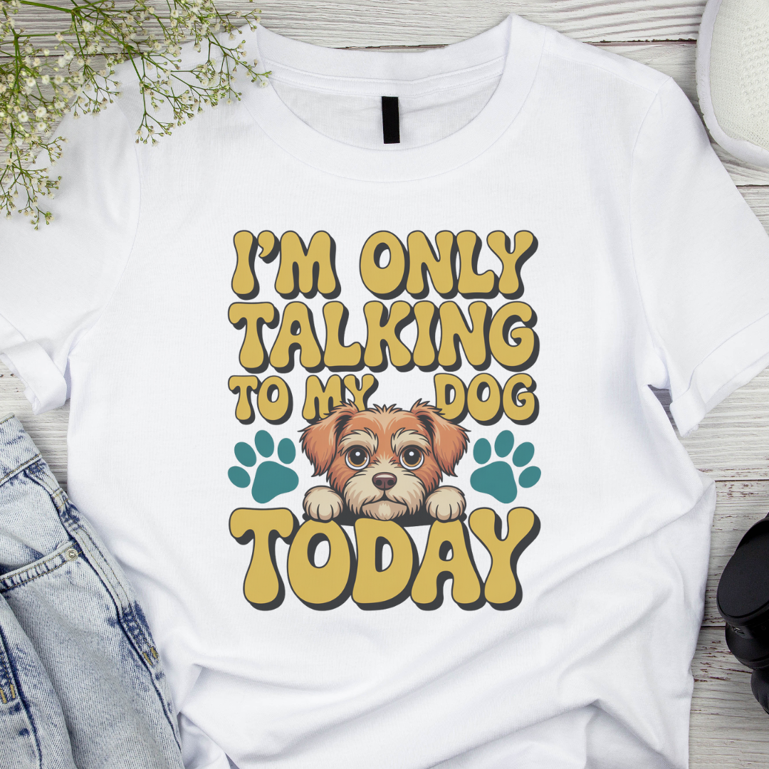 White t-shirt with a dog graphic and text 'I'm only talking to my dog today' on a wooden surface.