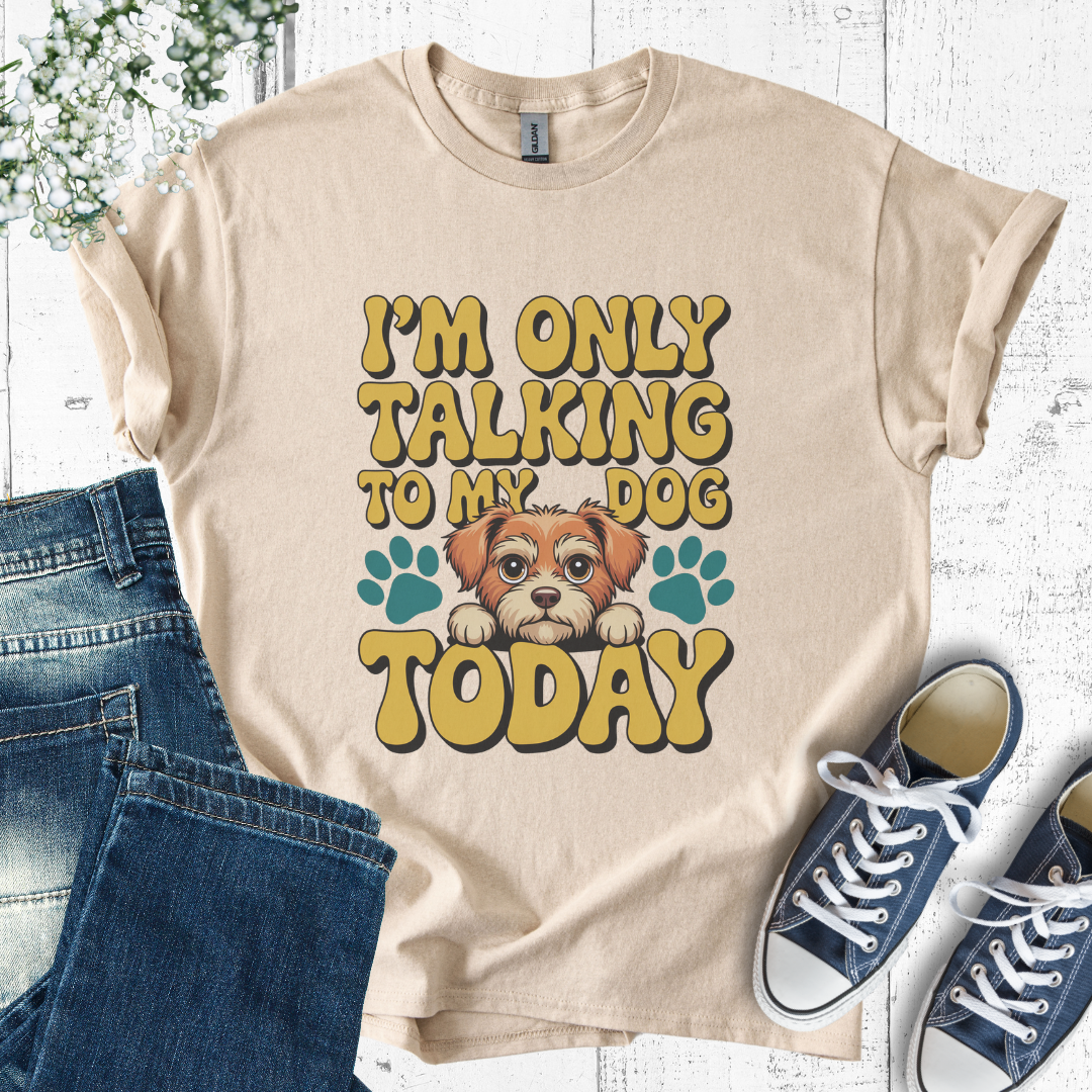Beige t-shirt with a dog graphic and text, paired with jeans and sneakers on a light wooden background.