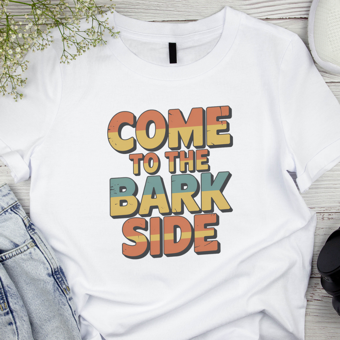 White t-shirt with 'Come to the Bark Side' text on a wooden surface with denim jeans and flowers.