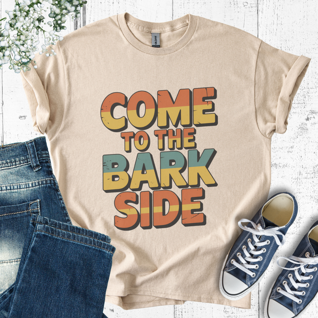Beige t-shirt with 'COME TO THE BARK SIDE' text, paired with jeans and sneakers on a light wooden surface.