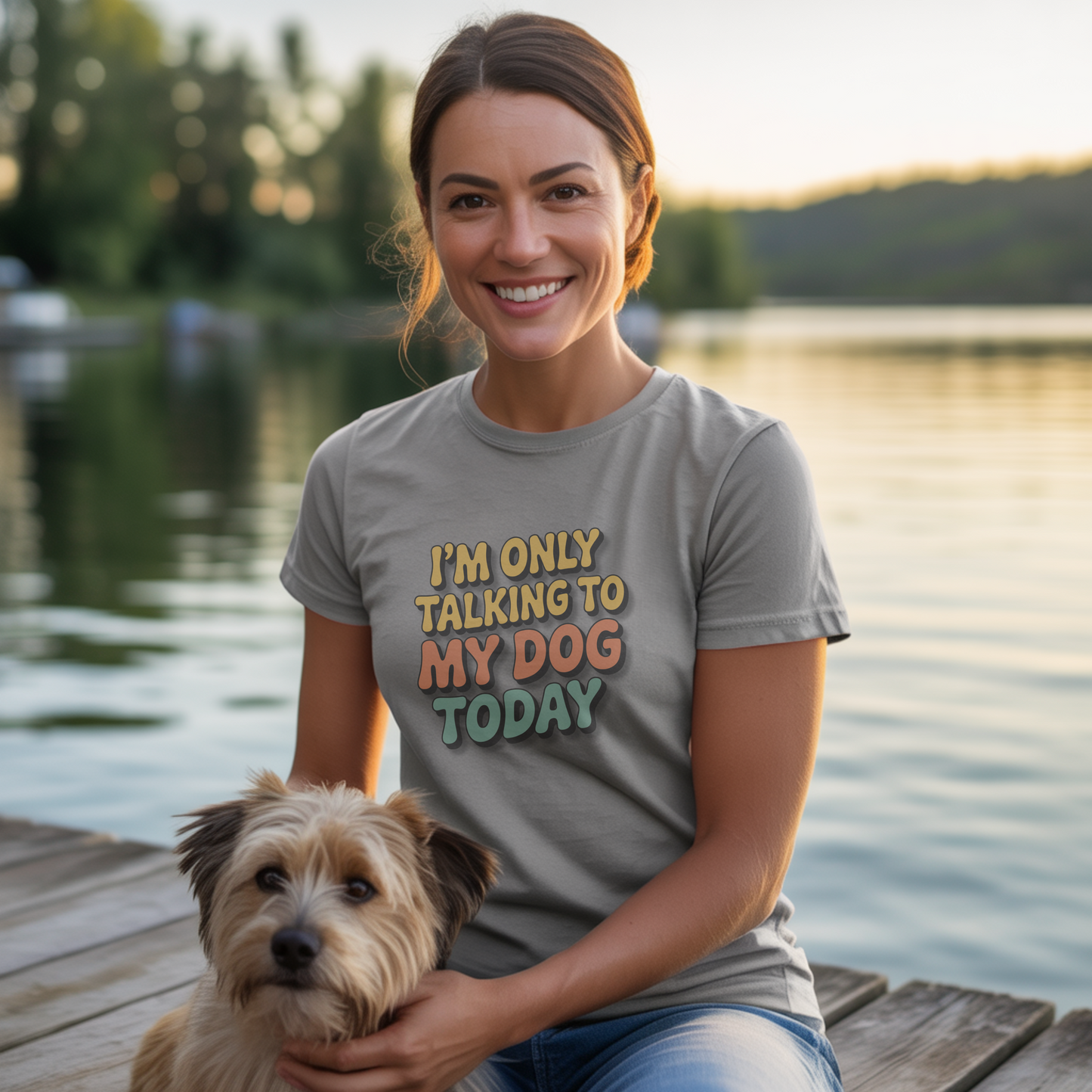 Woman wearing a t-shirt with 'I'm only talking to my dog today' text, standing on a dock by a lake.