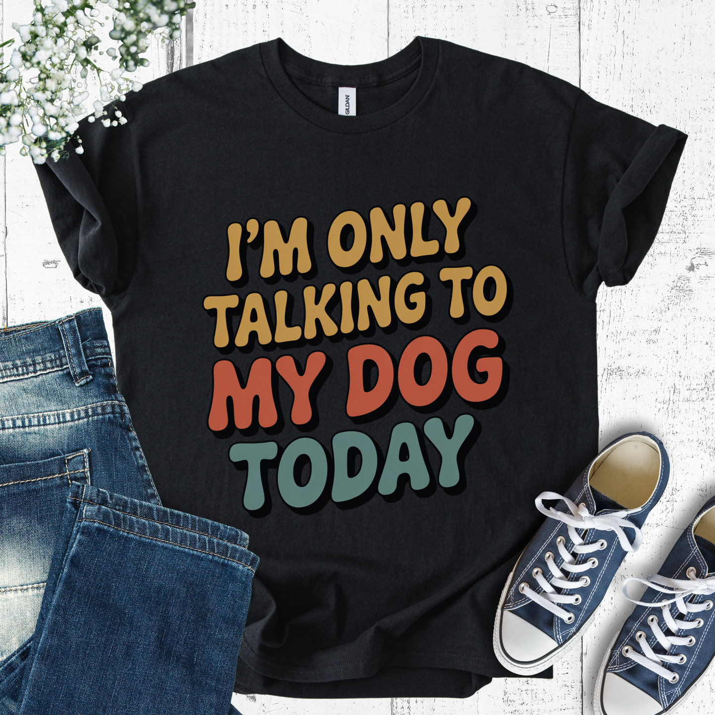 Black t-shirt with colorful text 'I'm only talking to my dog today' on a white background with jeans and sneakers.